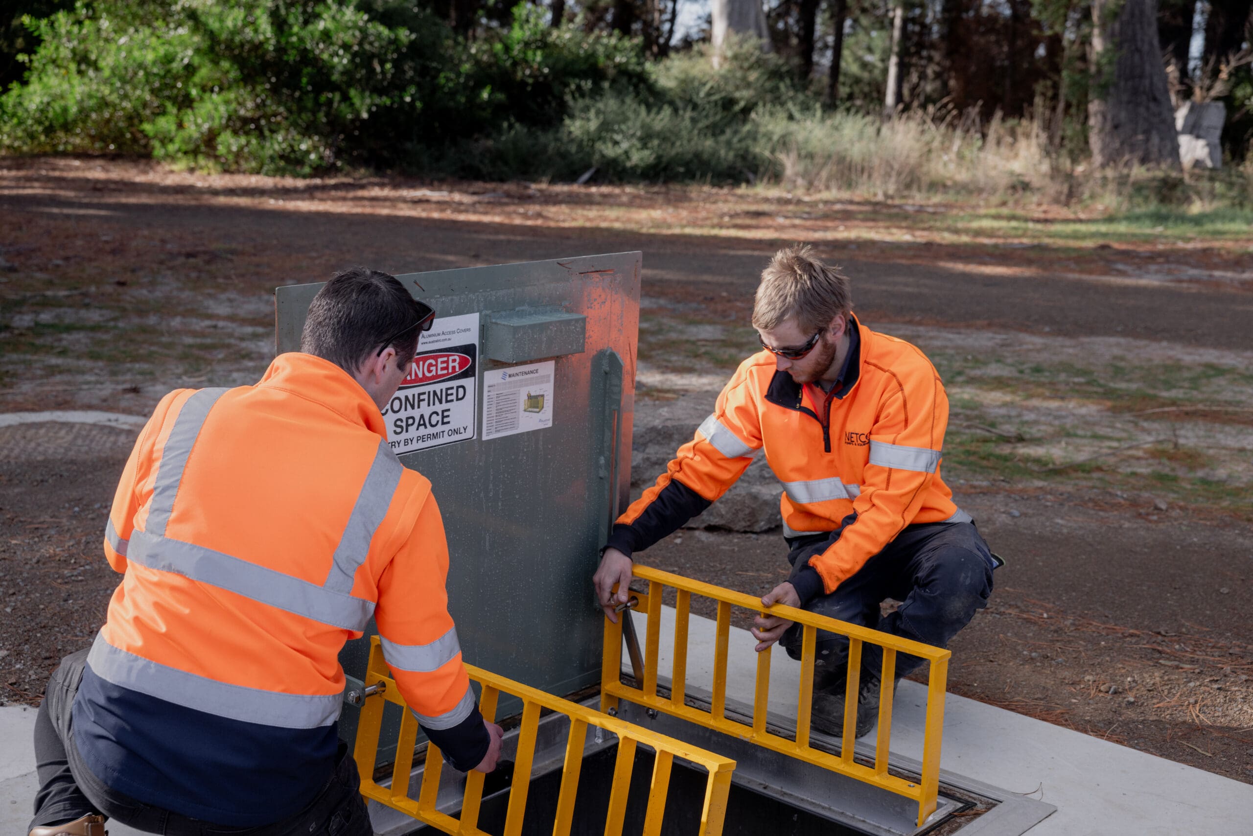 Workers installing safety barrier near confined space.